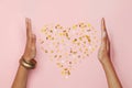 Fairy female hands and heart of falling confetti stars on pink background