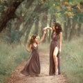 Fairy mother deer on path spinning her daughter on a forest trail, wearing long brown dresses, showing her charming leg Royalty Free Stock Photo