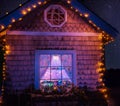 Fairy-tale house in the lights and a luminous window with a Christmas tree . Night photo. Royalty Free Stock Photo