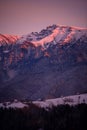 Fairy tale landscape with a rocky mountain full of snow at sunset. A village of traditional Romanian old houses over a valley. Royalty Free Stock Photo