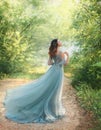 Fairy tale princess in light summer blue, turquoise dress standing in park. Happy Woman walks towards wind, graceful