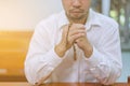 A faithful Asian young male hands in prayer gesture sitting alone on sofa at church pray and hope for good luck, success, forgiven