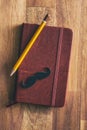 Fake black mustache on diary with pencil.