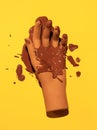 Fake hand and cacao cream on yellow background. Minimalist creative wallpaper. Chocolate addict concept