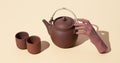 Fake hand holding clay teapot on beige background. Minimal stilll life isometric art