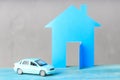 A fake paper cut house on a dark gray background, a car is standing next to the house