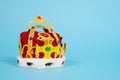 Fake plastic royal crown decorated with fake gems, fur and red cloth on blue background, front view, copy space. Symbol Royalty Free Stock Photo
