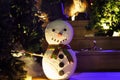 Fake snowman at the night time surrounded by Christmas trees