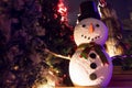 Fake snowman at the night time surrounded by Christmas trees