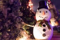 Fake snowman at the night time surrounded by Christmas trees