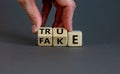 Fake or true symbol. Businessman flips wooden cubes and changes the word `fake` to `true` or vice versa. Beautiful grey backgr Royalty Free Stock Photo