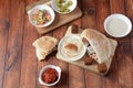 Falafel in pita bread with vegetable salad, harissa sauce, humus, tahini on wooden background.