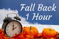 Fall Back 1 hour message with fall leaves, alarm clock, and pumpkins with sky Royalty Free Stock Photo