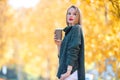Fall concept - beautiful woman drinking coffee in autumn park under fall foliage Royalty Free Stock Photo