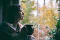 Fall melancholy mood concept. Sadness depressed woman sitting near window and looking at autumn landscape outside in rainy day