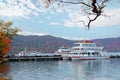 Fall scenery of beautiful Lake Towada, with sightseeing boats parking by the docks & colorful maple trees on the lakeside mountain