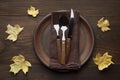 Fall table setting for Thanksgiving dinner on rustic wooden table with yellow maple leaves.