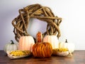 Fall themed decor, a wooden wreath with little pumpkin gourds and fall corn with an orange pumpkin in the center on a wooden