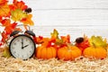 Fall time scene with alarm clock and orange pumpkins and fall leaves on straw hay with weathered whitewashed wood Royalty Free Stock Photo