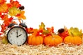 Fall time scene with alarm clock and orange pumpkins and fall leaves on straw hay isolated over white Royalty Free Stock Photo