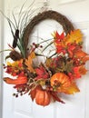 Fall wreath with artificial leaves and pumpkins hanging on a door Royalty Free Stock Photo