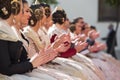 Falleras seated clapping at a public event in the city. Group of unfocused falleras