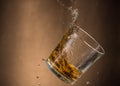 Falling glass with whiskey and spray on a brown background