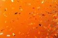 falling gold glitter foil confetti, on orange background, holiday and festive fun concept Royalty Free Stock Photo