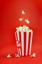 Falling popcorn in a striped cardboard box on a red background, vertical view