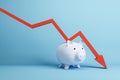 Falling red chart arrow with piggy bank on blue background. Economic recession, losing savings concept. Royalty Free Stock Photo