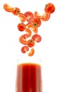 Falling sliced tomatoes in glass of tomato juice on white background