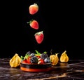 Falling strawberry into porceline pot with mix berries on dark marble background Royalty Free Stock Photo