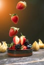 Falling strawberry into porceline pot with mix berries on dark marble background Royalty Free Stock Photo