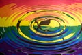 A falling water drop reflected in the circular waves from a splash and the colours and logo of Extinction Rebellion Gay Pride flag Royalty Free Stock Photo