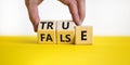 False or true symbol. Businessman turns wooden cubes and changes the word false to true or vice versa. Beautiful yellow table, Royalty Free Stock Photo