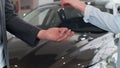 Famale hand gives a car keys to male hand in the car dealership close up. Unrecognized auto seller and a woman who