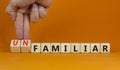 Familiar or unfamiliar symbol. Businessman turns wooden cubes changes the word unfamiliar to familiar. Beautiful orange table