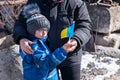 Upset Ukrainian boy with his grandmom, with bue yellow flag, protesting war conflict.