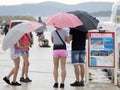 Familly holding umbrellas in front of boat excursion buildbords on a rainy summer day by the sea