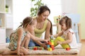 Family activities in the children room. Mother and her kids sitting on the foor playing