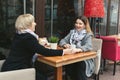 Family, an adult mother and daughter are sitting at a wooden table in a cafe on the street, looking at each other Royalty Free Stock Photo