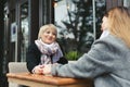 Family, an adult mother and daughter are sitting at a wooden table in a cafe on the street, looking at each other Royalty Free Stock Photo