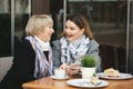 Family, an adult mother and daughter are sitting at a wooden table in a cafe on the street, looking at each other Royalty Free Stock Photo