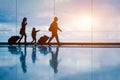 Family at airport travelling with young child and luggage walking to departure gate, girl pointing at airplanes through window,