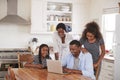 Family Around Kitchen Table Booking Vacation On Laptop Together