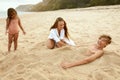 Family On Beach. Mother Burying Son In Sand And Laughing. Little Girl Standing Near Young Woman And Boy. Royalty Free Stock Photo