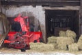Family of black cats lounging on red farm machine and bales of hay in an open barn