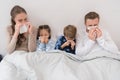 Sick parents ans children lying in a bed and blowing noses