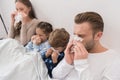 Sick parents with son and daughter lying in a bed and blowing noses