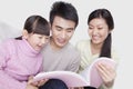 Family bonding together, smiling and reading on the sofa, looking down at book, studio shot